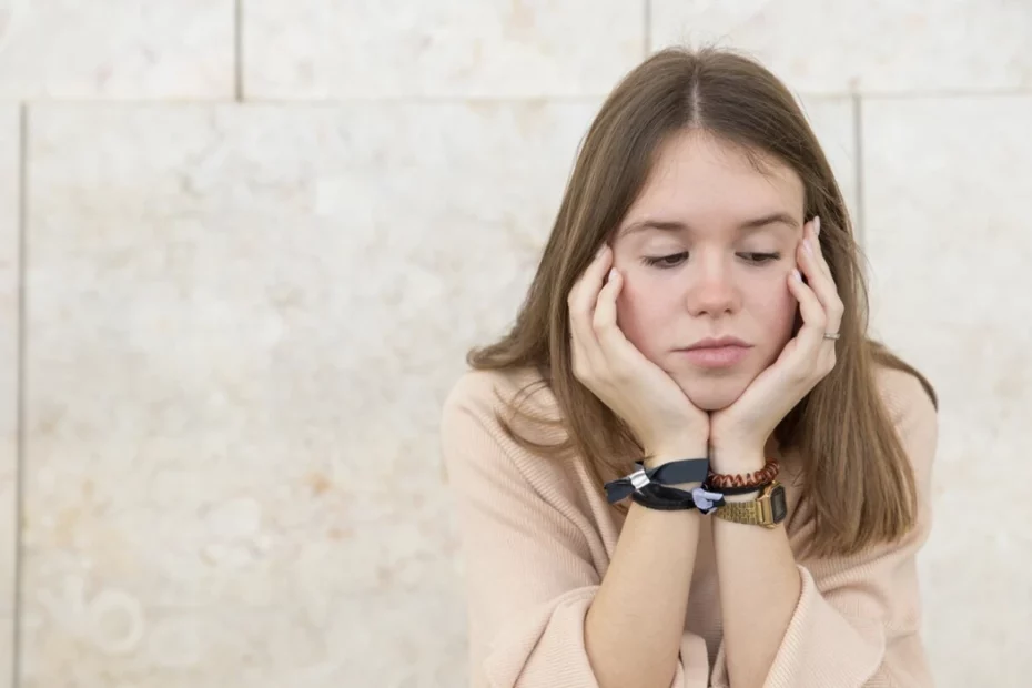 Uma jovem está sentada num muro com as mãos na cabeça, refletindo os desafios da puberdade.