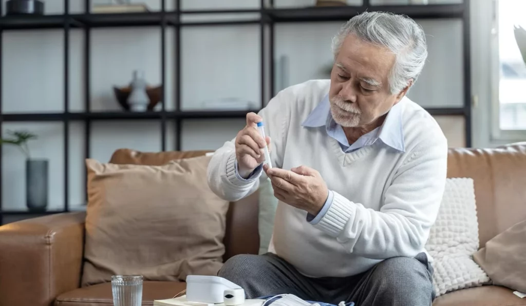 Um idoso com diabetes está sentado em um sofá medindo a sua glicemia com um aparelho.