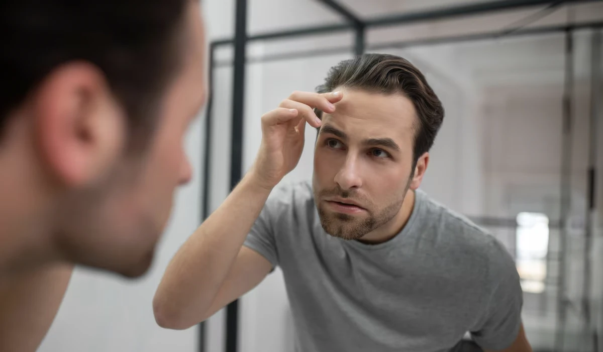 Homem se olhando no espelho verificando o cabelo após o tratamento com finasterida